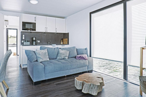 Modern living room on houseboat Floating 33 - LP 16, with blue sofa, kitchen, and large windows over the water.