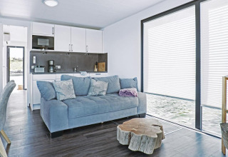 Moderne woonkamer op woonboot Floating 33 - LP 16 met blauwe bank, keuken en grote ramen met waterzicht.