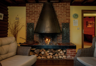 Gemütliches Wohnzimmer mit Kamin, Korbmöbeln und Holzvorrat im Chalet Les Muguets in Belgien.
