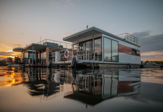 Houseboat moderno a Zehdenick sull’acqua calma al tramonto, con splendidi riflessi e atmosfera serena.