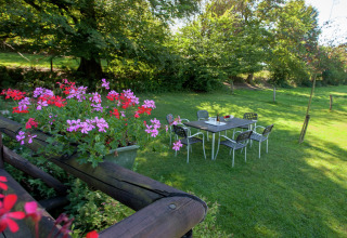 Blumen im Vordergrund und ein Gartentisch auf einer Wiese beim Chalet ‘Les Muguets’ in Belgien.
