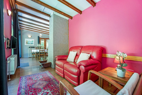 Area soggiorno del lodge Manonfa in Belgio con divano rosso, parete rosa e vista sulla sala da pranzo.