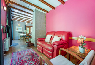Area soggiorno del lodge Manonfa in Belgio con divano rosso, parete rosa e vista sulla sala da pranzo.