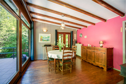 Eetkamer bij lodge Manonfa in België, houten balken, roze muur en uitzicht op het groene bos.