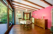 Sala da pranzo al lodge Manonfa in Belgio, travi in legno, parete rosa e grandi finestre sul verde.