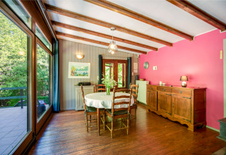 Eetkamer bij lodge Manonfa in België, houten balken, roze muur en uitzicht op het groene bos.