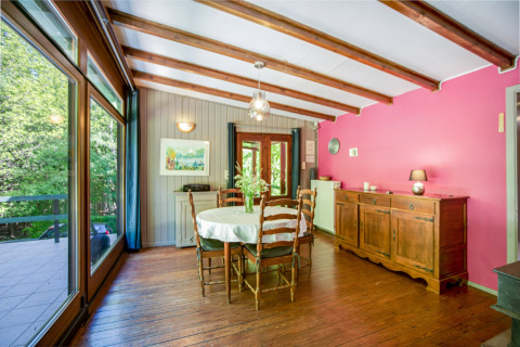 Sala da pranzo al lodge Manonfa in Belgio, travi in legno, parete rosa e grandi finestre sul verde.