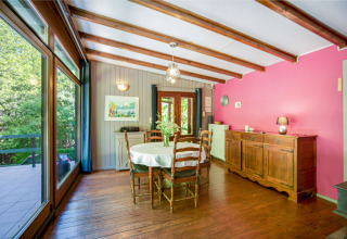 Sala da pranzo al lodge Manonfa in Belgio, travi in legno, parete rosa e grandi finestre sul verde.