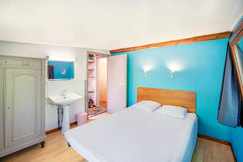 Lichte kamer met tweepersoonsbed, blauw accentmuur, lavabo en kast bij Manonfa in België.