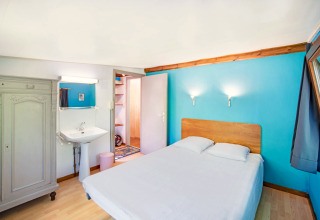Lichte kamer met tweepersoonsbed, blauw accentmuur, lavabo en kast bij Manonfa in België.
