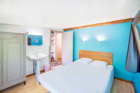 Camera luminosa con letto matrimoniale, parete blu, lavandino e armadio al Manonfa lodge in Belgio.