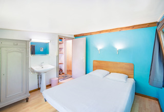Camera luminosa con letto matrimoniale, parete blu, lavandino e armadio al Manonfa lodge in Belgio.