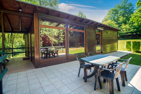 Buiten eetruimte aan Manonfa-lodge in België met tafel, stoelen, grote ramen en zicht op bomen