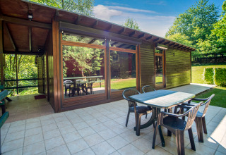 Buiten eetruimte aan Manonfa-lodge in België met tafel, stoelen, grote ramen en zicht op bomen