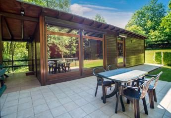 Zona pranzo esterna al lodge Manonfa in Belgio con tavolo, sedie e ampie finestre circondate da alberi