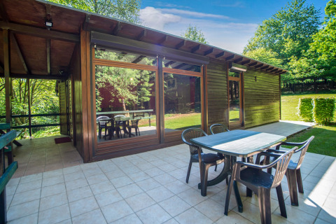 Zona pranzo esterna al lodge Manonfa in Belgio con tavolo, sedie e ampie finestre circondate da alberi