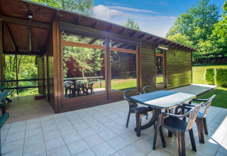 Zona pranzo esterna al lodge Manonfa in Belgio con tavolo, sedie e ampie finestre circondate da alberi