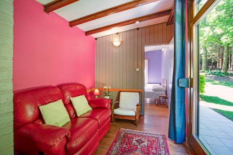 Lichte zithoek in Manonfa-lodge te België met rode zetel, houten vloer en zicht op de tuin.
