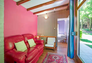 Luminoso soggiorno presso il lodge Manonfa in Belgio con divano rosso, pavimento in legno e vista giardino.
