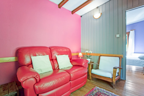 Lodge Manonfa in Belgio, divano rosso, sedia in legno, pareti colorate e vista sulla camera.