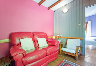 Lodge Manonfa in Belgio, divano rosso, sedia in legno, pareti colorate e vista sulla camera.