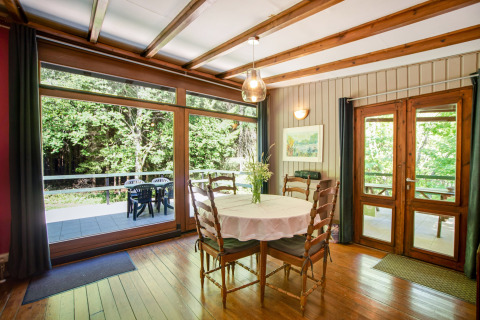 Sala da pranzo nel lodge Manonfa in Belgio, tavolo in legno, grandi finestre e vista sul bosco.