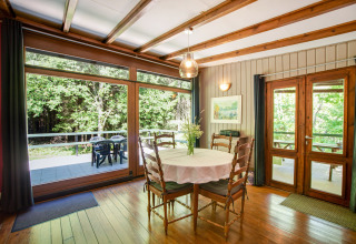 Sala da pranzo nel lodge Manonfa in Belgio, tavolo in legno, grandi finestre e vista sul bosco.