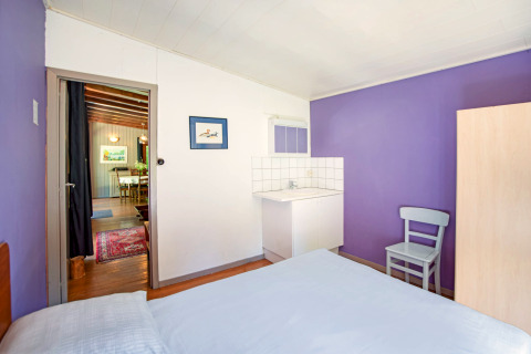 Lichte kamer met paarse muren, wastafel, stoel en zicht op eetruimte in Manonfa-lodge in België.