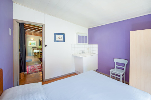 Stanza luminosa con pareti viola, lavandino, sedia e vista sulla sala da pranzo nel lodge Manonfa in Belgio.