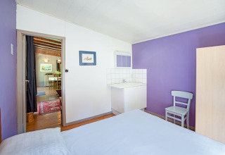 Stanza luminosa con pareti viola, lavandino, sedia e vista sulla sala da pranzo nel lodge Manonfa in Belgio.