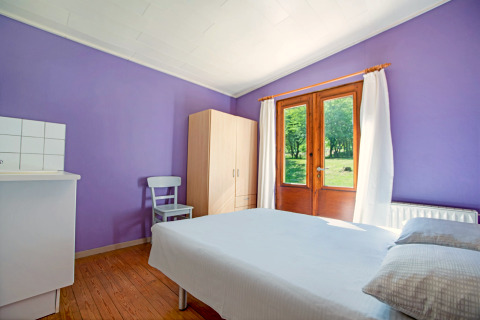 Lichte kamer met paarse muren, tweepersoonsbed en tuinzicht bij Manonfa lodge in België.