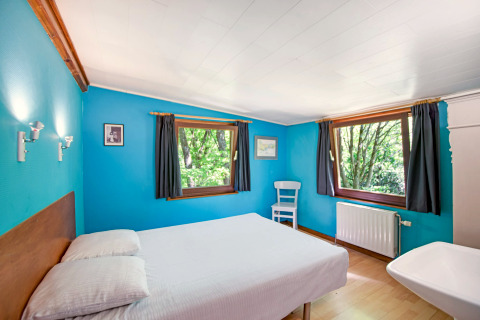 Lichte kamer in de Manonfa-lodge in België met blauwe muren, tweepersoonsbed en uitzicht op de natuur.