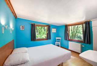 Lichte kamer in de Manonfa-lodge in België met blauwe muren, tweepersoonsbed en uitzicht op de natuur.