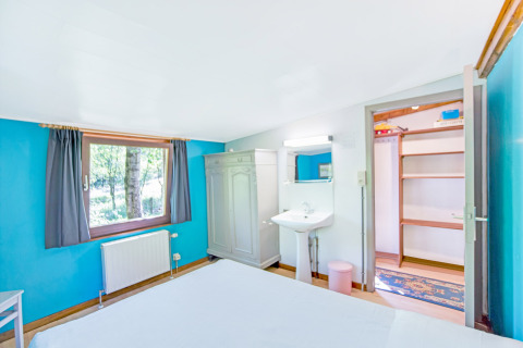 Camera luminosa al lodge Manonfa in Belgio, con pareti blu, finestra, armadio, lavandino e scaffali aperti.