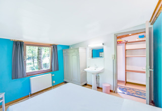 Camera luminosa al lodge Manonfa in Belgio, con pareti blu, finestra, armadio, lavandino e scaffali aperti.
