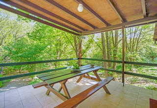 Terrazza coperta alla lodge Manonfa con tavolo da picnic, immersa nel verde in Belgio.