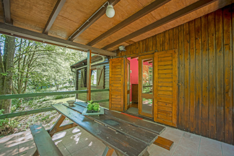 Veranda in legno con panca e vista sul bosco all’ingresso del lodge Manonfa in Belgio.