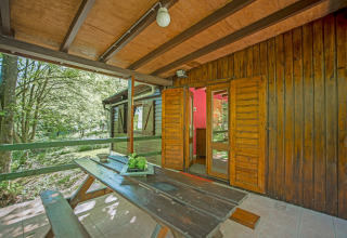 Veranda in legno con panca e vista sul bosco all’ingresso del lodge Manonfa in Belgio.