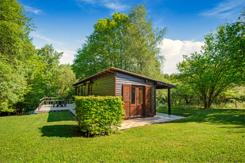 Het Manonfa-lodge in België, omringd door groene bomen en gras onder een heldere blauwe lucht.