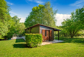 Het Manonfa-lodge in België, omringd door groene bomen en gras onder een heldere blauwe lucht.