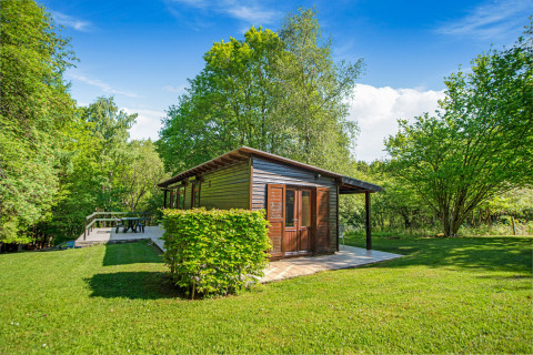 Il lodge Manonfa in Belgio circondato da alberi verdi e prato sotto un cielo limpido e azzurro.