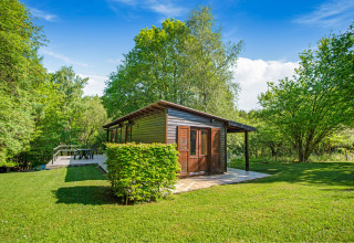 Il lodge Manonfa in Belgio circondato da alberi verdi e prato sotto un cielo limpido e azzurro.