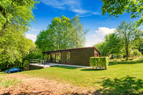 De Manonfa-lodge in België, gelegen tussen het groen, omringd door bomen en een blauwe lucht.