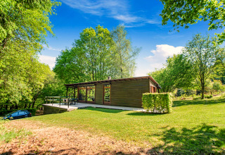 De Manonfa-lodge in België, gelegen tussen het groen, omringd door bomen en een blauwe lucht.