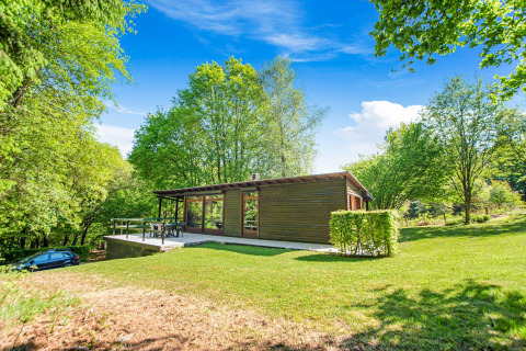 Lodge Manonfa in Belgio, immerso nel verde lussureggiante, con alberi e cielo azzurro.
