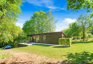 Lodge Manonfa in Belgio, immerso nel verde lussureggiante, con alberi e cielo azzurro.