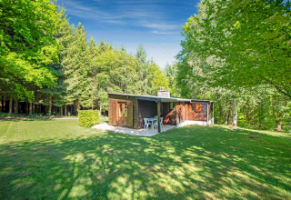Lodge Manonfa in België, omgeven door groene bomen en gras, schijnend in het zonlicht en open lucht.