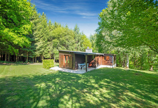 Lodge chiamato Manonfa in Belgio, circondato da alberi verdi e prato sotto un cielo azzurro luminoso.