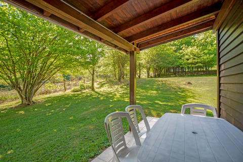 Zicht vanop het terras van lodge Manonfa in België met plastieken tafel, stoelen en een groene tuin.
