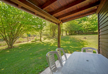 Vista dal lodge Manonfa in Belgio, terrazza con tavolo e sedie di plastica, prato e alberi verdi.
